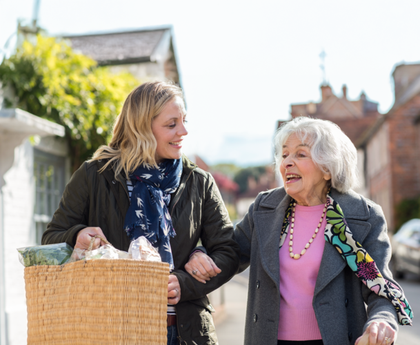 Eine jngere Frau trgt die Einkufe von einer lteren Frau und begleitet sie.